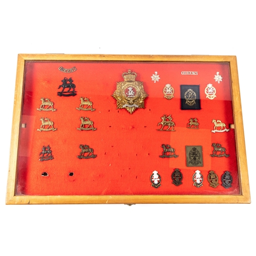 267 - A framed display of badges of the Queen's (Ryl West Surrey Regt), including ERII bandsman's helmet p... 