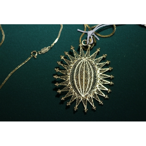 41 - An 18K gold  hallmarked chain with a large filigree sunburst style pendant with a small building to ... 