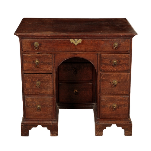 165 - A GEORGE I OAK KNEEHOLE DESK early 18th century, the shaped top over an arrangement of short drawers... 