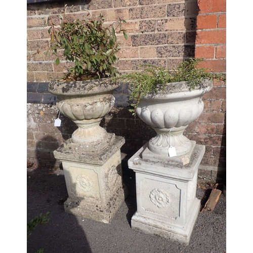 7 - A PAIR OF RECONSTITUTED STONE GARDEN URNS on plinths 80cm high