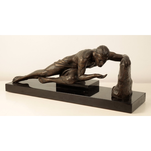 142 - A BRONZE-EFFECT ART DECO STYLE SCULPTURE modelled as a male in recumbent pose with his left arm rest... 