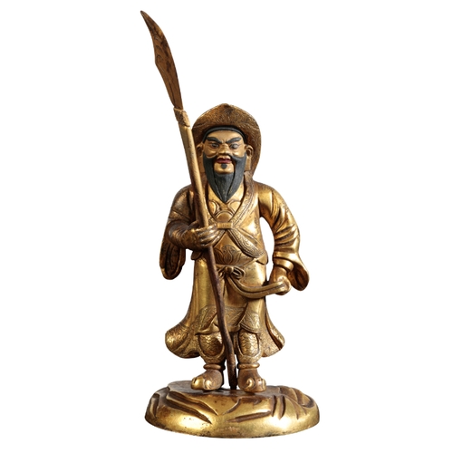 27 - A SINO-TIBETAN GILT BRONZE GUARDIAN FIGURE Qing or later, standing wearing a broad rimmed hat and ho... 