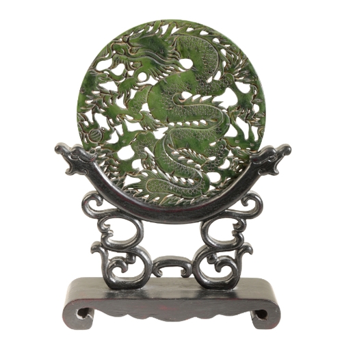 55 - A CHINESE DARK GREEN BOWENITE CIRCULAR PLAQUE mounted on a wooden stand as a table screen, 21cm high