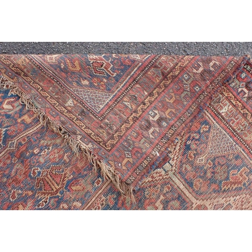 570 - AN ANTIQUE SHIRAZ CARPET woven in colours and white with two links rows of seven lozenge medallions,... 