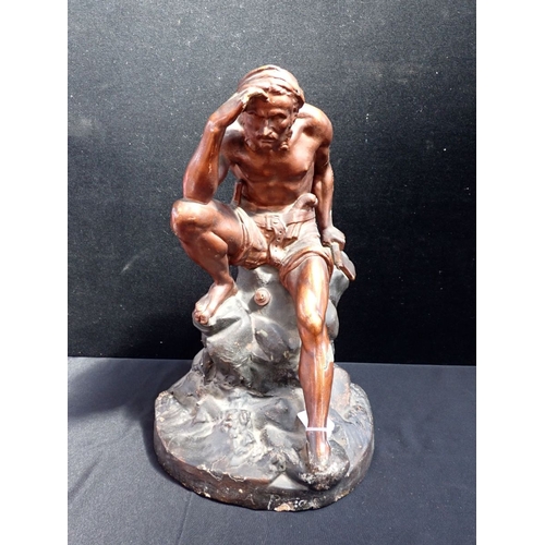 18 - AN EARLY 20TH CENTURY BRONZED PLASTER FIGURE of an armed man in shorts, seated on rocks 49cm high (a... 