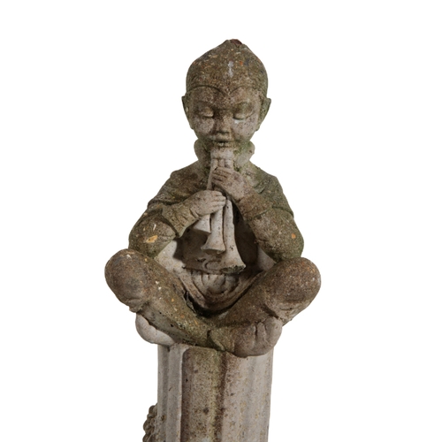 12 - A RECONSTITUTED STONE FIGURE OF A BOY seated playing pipes on top of a fluted column, on a moulded s... 