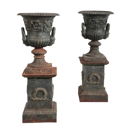 35 - A PAIR OF CAST IRON URNS each decorated with foliate banding, above turned pedestal bases, mounted o... 