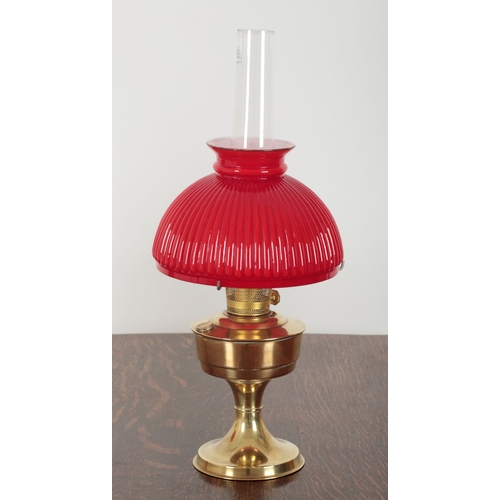 142 - A PAIR OF 20TH CENTURY ALADDIN BRASS TABLE OIL LAMPS with reeded red and white cased glass shades an... 