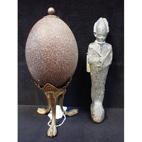 258 - AN ARCHAIC EGYPTIAN STONE TOMB FIGURE 20cm long, and an emu egg curiosity, on gilt stand (2)