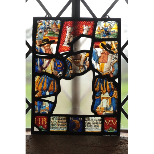 71 - A SWISS STAINED GLASS PANEL with a soldier on horseback beside a lady holding a flagon above a coat ... 