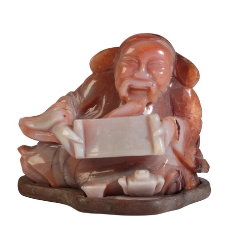 51 - A CHINESE CARVED AGATE FIGURE OF A RECLINING SCRIBE

20th century, 8cm high x 9.5cm wide, on a hardw... 