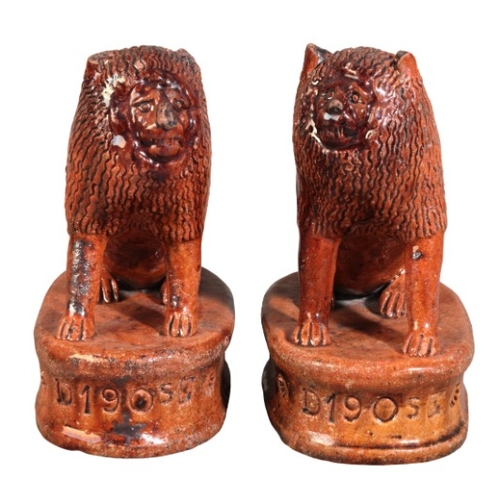 84 - A PAIR OF ENGLISH TREACLE-GLAZED TERRACOTTA LIONS

each impressed 'D 1905 E', probably Staffordshire... 