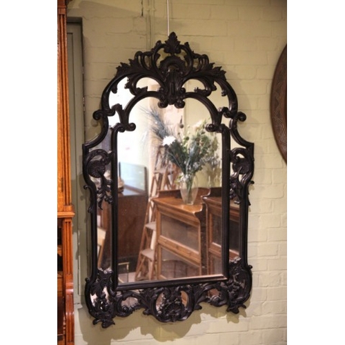 910 - AN EBONISED WOOD WALL MIRROR OF ROCOCO STYLE

with pierced shaped frame and plain mirror plate, 140c... 