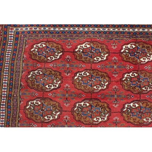 527 - A BOKHARA CARPET OF TURKOMAN STYLE

woven in colours with five rows of thirteen guls, on a cochineal... 