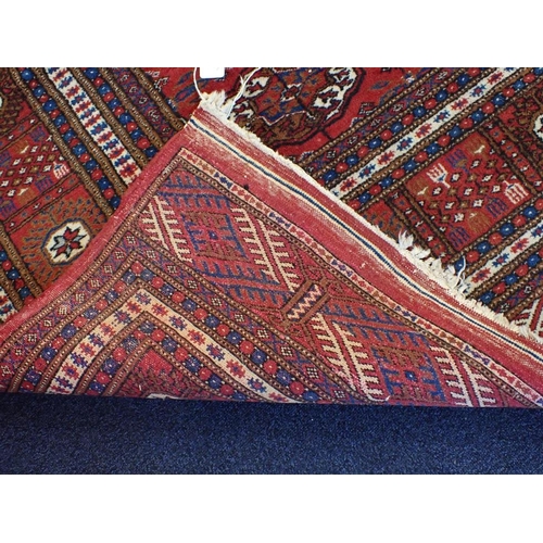 527 - A BOKHARA CARPET OF TURKOMAN STYLE

woven in colours with five rows of thirteen guls, on a cochineal... 