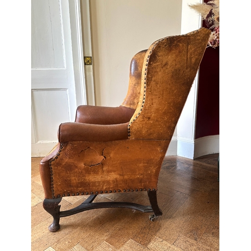 25 - A MAHOGANY WINGBACK ARMCHAIR

stamped '34544' to a back leg, with distressed leather covers, on shor... 