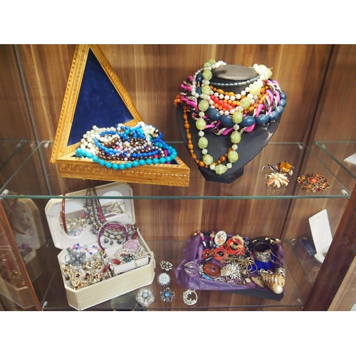 67 - Four shelves full of costume jewellery including beads, brooches, bangles, earrings etc.
