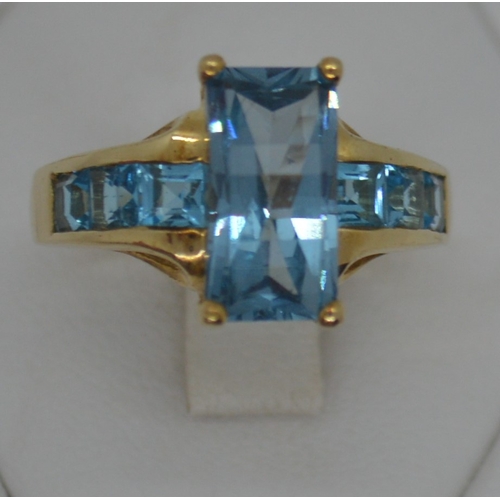 120 - 9ct yellow gold ring with faceted rectangular blue stone - possibly topaz, with co-ordinating square... 