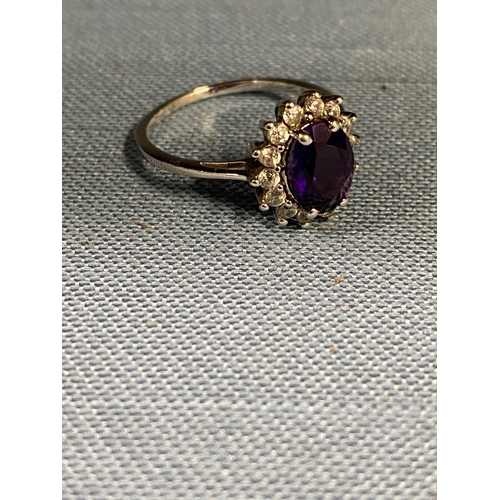 129 - A ladies cluster ring, marked 10ct. Central oval purple stone surrounding clear stones, hallmarked 3... 