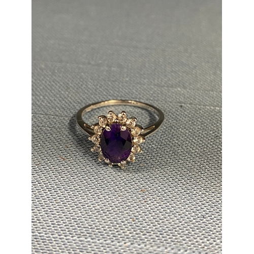 129 - A ladies cluster ring, marked 10ct. Central oval purple stone surrounding clear stones, hallmarked 3... 