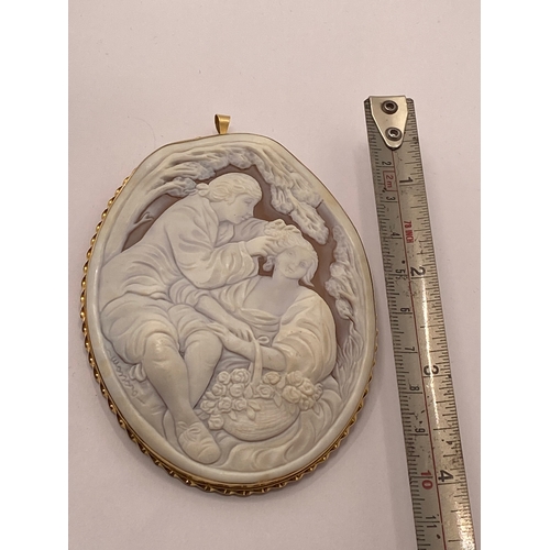 113 - A large 15ct yellow gold cameo pendant / brooch, depicting romantic scene of man placing flower in h... 