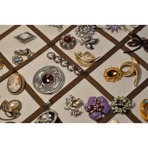 29 - A board containing a selection of various brooches/ pin badges in various shapes and designs