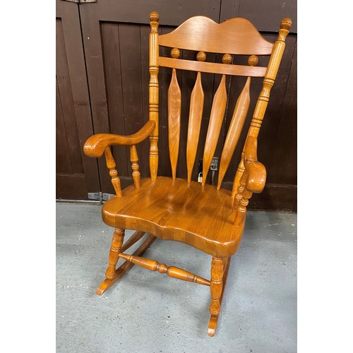 147A - A large solid wood rocking chair with tall slat back backrest design and turned supports.