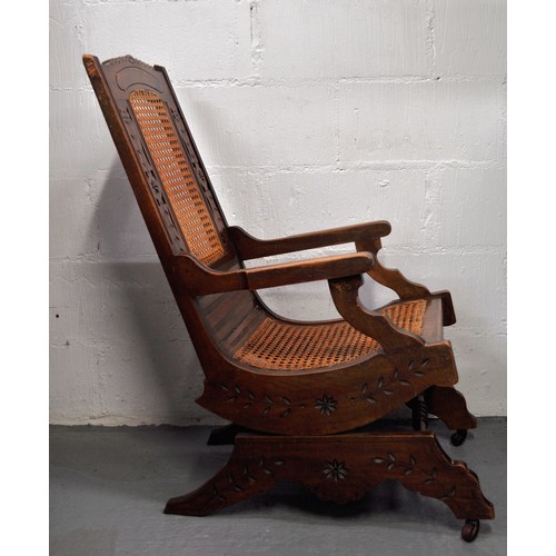 104 - Antique American style coil sprung cane rocking/rocker chair with carved detailing