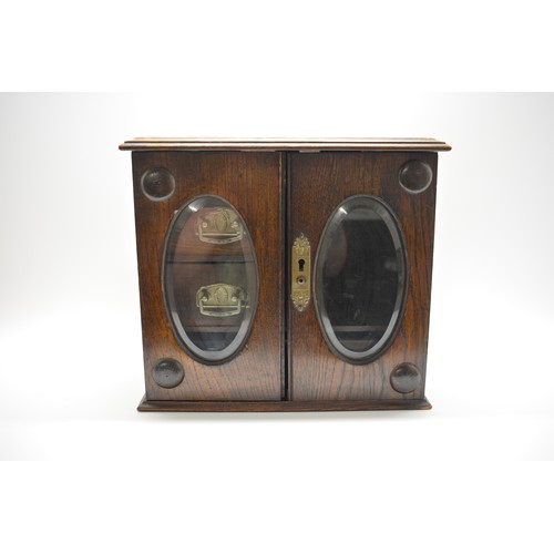 57 - Oak Smokers Cabinet adorned with bevelled oval glass, 2 internal drawers with ornate handles, no key... 