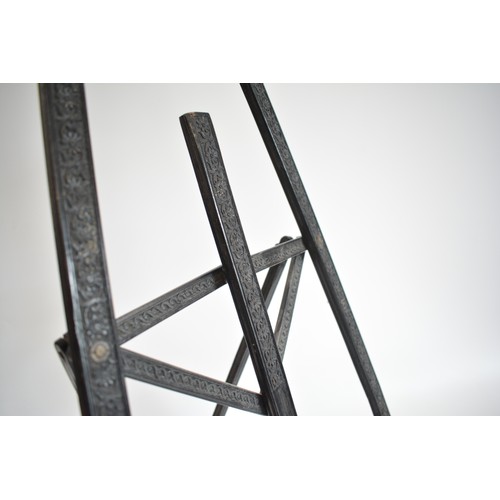 63 - Vintage ebonised Easel with carved scroll foliate design. size 40cms widest point, 62 cms tall