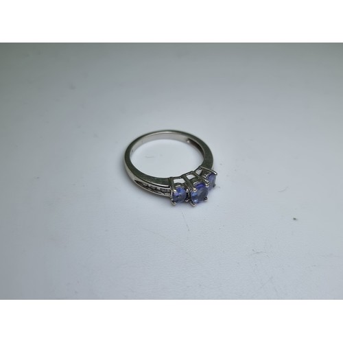 458 - A three stone 9 carat white gold tanzanite ring with diamond set shoulder mount. Weight 2.1g, size H... 
