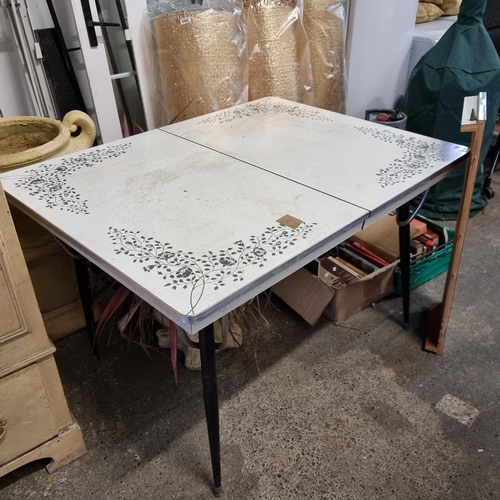 768 - A charming mid century  formica kitchen table with a black floral motif. With a central leaf for ext... 