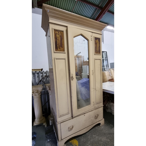 769 - A large, vintage cream wardrobe. With mirrored central door and two glazed relief panels depicting a... 