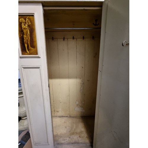 769 - A large, vintage cream wardrobe. With mirrored central door and two glazed relief panels depicting a... 