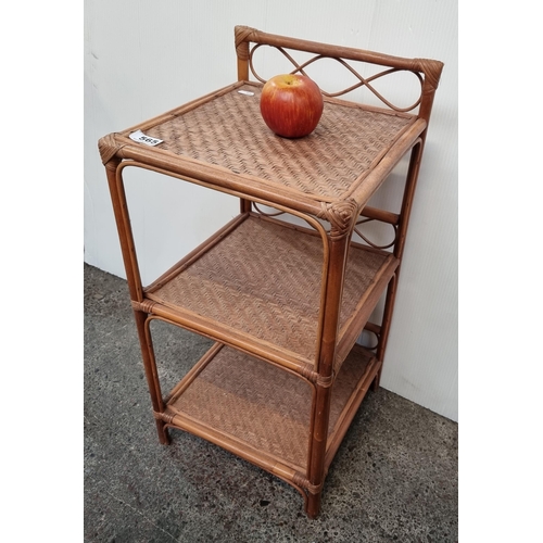 565 - A neat sized three-tier cane and wicker shelving unit.