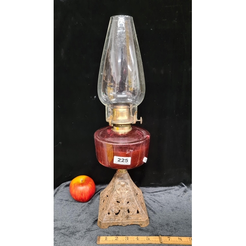 225 - A tall oil lamp with a cranberry glass font, intricately worked metal base, fluted glass shade and b... 