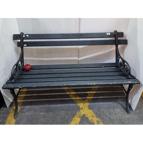398 - A vintage two-seater garden bench with cast metal bench ends and wooded slats. In a black shade.