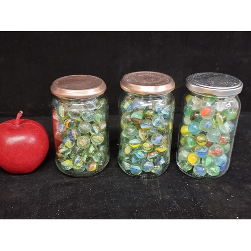 231 - Three jars of vintage glass marbles, with swirled cores. Two of the three jars contain marbles which... 