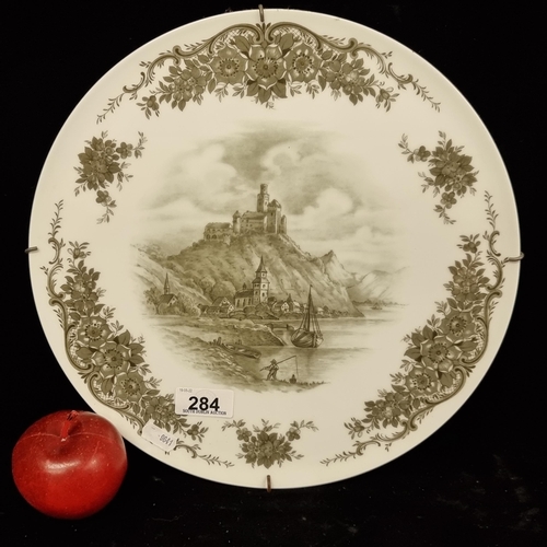 284 - A large ceramic decorative plate, featuring a central vignette of a Rheingau castle, surrounded by a... 