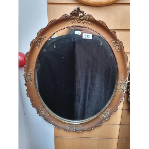 313 - A oval wall hanging mirror with with an ornate copper toned frame.