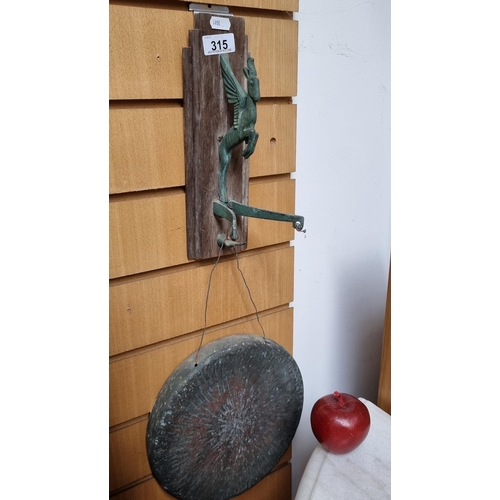 315 - An antique copper dinner gong which hangs from a Pegasus shaped wall mount on a wooden plaque.