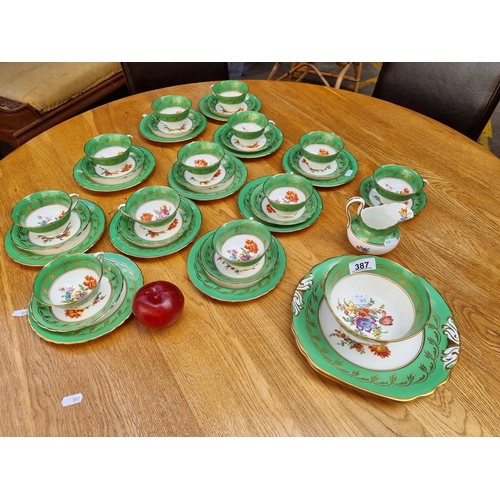 387 - Thirty nine pieces of china tableware with a bright green and gilt border decorated with a floral mo... 