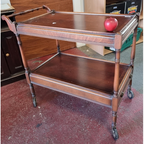 607 - An antique wooden drinks trolley with two tiers, turned wood legs with castors and handle to side. H... 