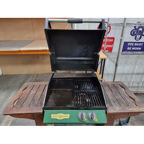 769 - An Australian gas-powered bbq grill with wooden frame and castors for easy movement. With a cylinder... 