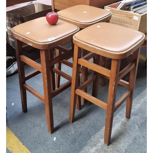 370 - A collection of three matching mid-century modern bar stools with tan leather cushioned seats.