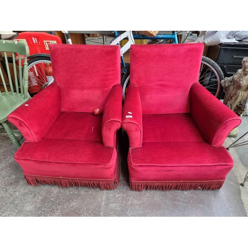 728 - A super retro pair of armchairs upholstered in deep plush scarlet with fringed apron all held on cas... 