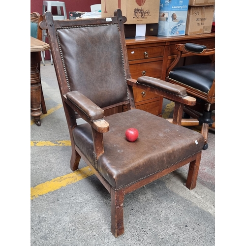 373 - An early 20th century heavy oak framed open armed chair with dark leather upholstery and stud detail... 