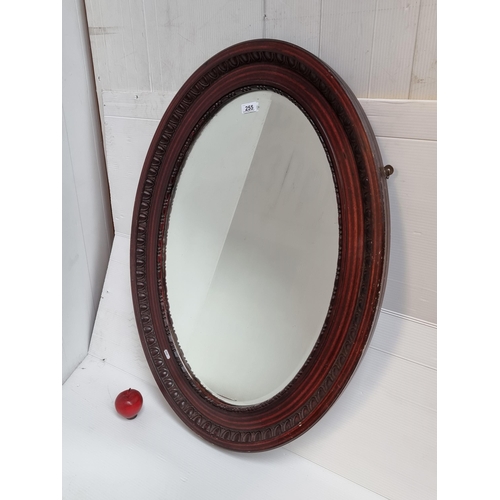 255 - A vintage oval bevelled mirror housed in a carved wooden frame. H94cm x W69cm