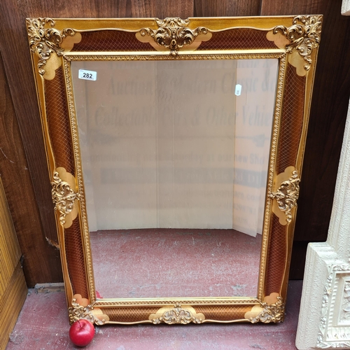 282 - A bevelled wall mirror framed with a gilt wood and bronze toned frame, featuring ornate detailing fo... 