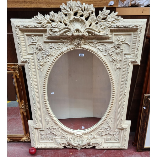 283 - A large, impressive oval wall mirror set into a highly lavish carved frame, with roses and vines in ... 